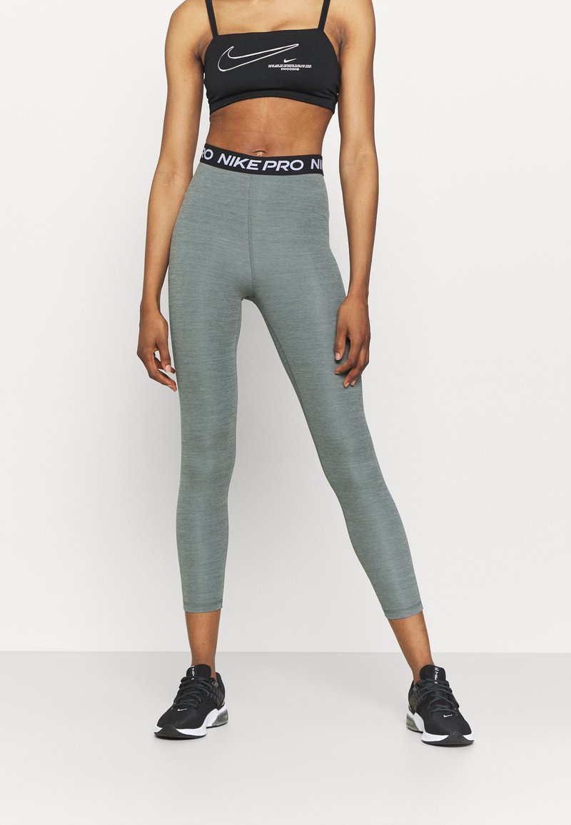 Leggings de sport gris avec une finition texturée, taille haute avec taille de Nike Pro, assortis à un soutien-gorge de sport noir de Nike et à des chaussures de course noires.