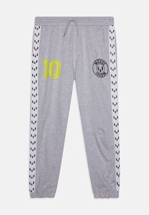 Graue Jogginghose mit weißen Seitenstreifen, die schwarze Logos zeigen, gelbe Nummer 10 auf dem linken Oberschenkel und rundes schwarzes Messi-Emblem auf dem rechten Oberschenkel.