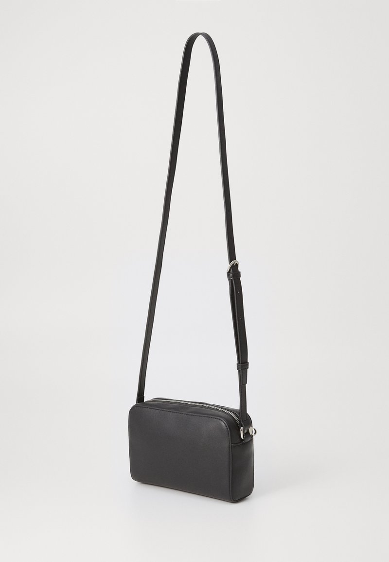 Sac bandoulière en cuir noir de forme rectangulaire, texture lisse, fermeture éclair et bandoulière réglable. Design simple et fonctionnel.