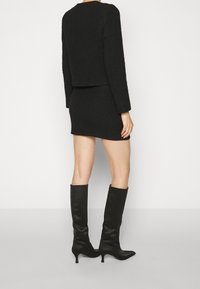 Zwarte cropped sweater en strakke minidress, beide met textuur. Gecombineerd met hoge, strakke zwarte laarzen. Eenvoudig ontwerp zonder zichtbare patronen.