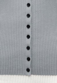 Ανοιχτό γκρι πλεκτό ύφασμα με κάθετη σειρά από επτά μαύρα κουμπιά τοποθετημένα ομοιόμορφα στη μέση.