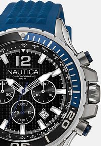 Nautica kroonimähis kell musta tekstuuriga kelladialiga, hõbedaste ja siniste aktsentidega, sinise kummirihmaga ja hõbedasest roostevabast terasest korpusega; veekindel kuni 100m.