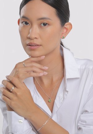 Les bijoux en argent sterling comprennent un pendentif vert, des boucles d'oreilles assorties et une bague en argent. Le modèle porte une chemise blanche à col, avec une peau lisse.