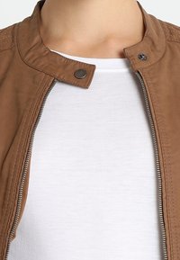 Giacca in pelle sintetica marrone con collare alto, zip frontale e chiusura con bottoni a pressione. Presenta una texture liscia e dettagli di cucitura.
