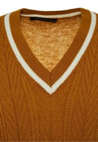 Pull en maille moutarde à col en V avec bordure blanche et motif à torsades.