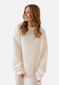 Przesadny biały sweatshirt wykonany z miękkiego materiału, z opadającymi ramionami, ściągaczami i wysokim kołnierzem. Gładka tekstura i prosty design.