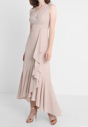 Sleeveless beige midi dress with pleated V-neck, asymmetrical ruffle detail, worn with metallic rose gold high-heeled sandals.