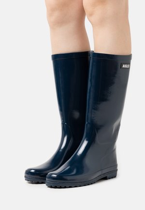 Bottes de pluie en caoutchouc de couleur marine avec une finition brillante, de conception hauteur genou, semelles durables avec un bon grip, et un petit logo sur le côté.