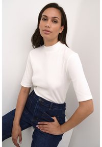 Vit ribbad kortärmad topp med hög krage, tillsammans med högmidjade blå jeans med framfickor och knappstängning.