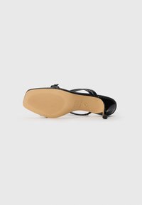Black high-heel sandal with a smooth patent finish, adjustable ankle strap, and a textured beige rubber sole. Sleek design with minimal detailing.