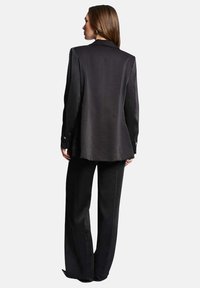 Blazer negro a medida con cierre de un botón y mangas largas, combinado con pantalones de pierna ancha a juego, que exhiben una textura suave.