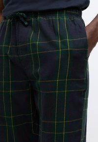 Herrens flannel pyjamasbyxor i mörkgrön och marinblå med rutmönster och gula accenter. Har en elastisk midja med dragsko.