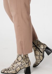 Enkellaarsjes met slangenprint in beige en bruin, voorzien van een spits toelopende neus en een blokhak. De broek is nauwsluitend, gemaakt van een zachte lichtroze stof met ritsen bij de zoom.