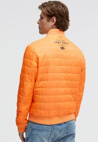 Gepolsterte orangefarbene Jacke mit gerippten Bündchen und Saum. Verfügt über einen hohen Kragen und Logodetails auf der Rückseite. Glatte Textur, lässiges Design.