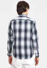 Geklede flanellen overhemd met blauwe, zwarte en witte kleuren; lange mouwen; knoopmanchetten; gebogen zoom; zachte textuur.