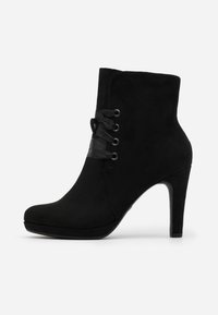 Botín negro de ante hasta el tobillo con punta afilada, tacón alto y cordones decorativos que presentan cintas de satén negro a través de ojetes plateados.