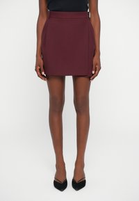 Burgundowa mini spódnica o gładkiej fakturze, średnio wysoko osadzonym pasie i bocznymi plisami, w połączeniu z czarnymi szpilkami w szpic.