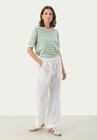 T-shirt à manches courtes rayé vert et beige associé à un pantalon en lin blanc ample avec poches et taille élastique. Baskets décontractées incluses.