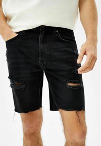Černé denimové šortky s odstřižením na přední části, se zadními třásněmi a designem s pěti kapsami. Upravený pas s klasickým knoflíkovým zapínáním.