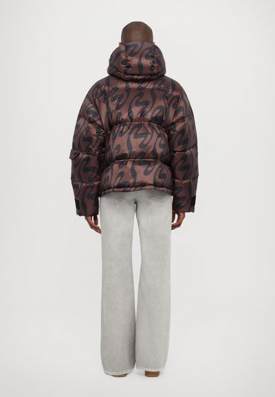 Puffer jacket in dark brown and black, with a shiny, patterned exterior. Features a hood, oversized fit, and elasticized cuffs. Worn with light gray jeans.