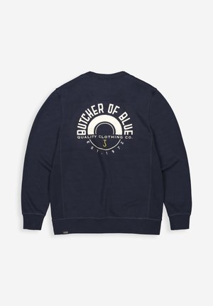 Marineblauwe sweatshirt met een ronde grafische ontwerp op de achterkant; met de tekst "BUTCHER OF BLUE" en "QUALITY CLOTHING CO." in crèmekleurige letters.