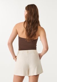 Débardeur ajusté marron avec des bretelles spaghetti associé à un short en lin couleur crème, offrant une coupe décontractée et une taille élastique.