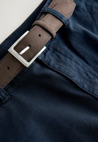 Pantalon bleu foncé texturé avec une ceinture en daim marron attachée par une boucle rectangulaire argentée.