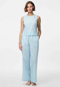 Svijetloplava bezrukavna bluzica s boxy krojem, u kombinaciji s odgovarajućim širokim hlačama koje imaju suptilan karirani uzorak i elastičnu ustru.