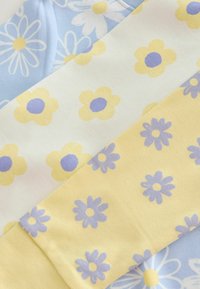 Drei gefaltete Stoffe mit Blumenmustern: blau mit weißen und gelben Gänseblümchen, weiß mit gelben Blumen und violetten Zentren, gelb mit violetten Blumen.