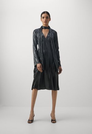 Must musta, läikiv kleit, mis on valmistatud siledast kangast, sügava V-kaelusega, pikad varrukad ja A-lõige, mis voolab sääre keskele.