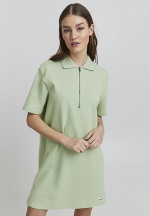 Polo jurk in lichtgroen, met korte mouwen, een ritskraag en een gestructureerde stof. Merklabel zichtbaar aan de zoom.