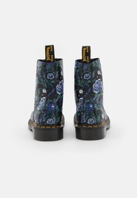 Zwarte enkellaarsjes met een bloemenpatroon in blauw en wit. Voorzien van een gestructureerde afwerking, een gele logo-label en contrasterende gele stiksels.