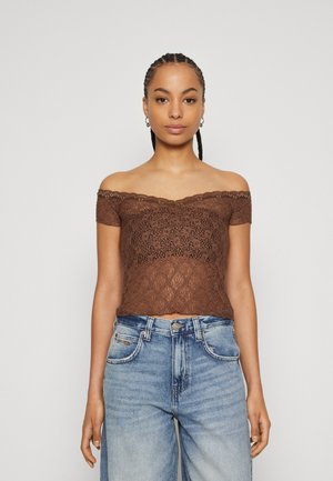 Hnedý čipkovaný top bez ramienok s krátkymi rukávmi, s volánovým lemom a kvetinovým vzorom, skombinovaný so svetlomodrými džínsy s vysokým pásom.