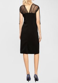 Černé šaty s průhlednými černými rukávy, designem V-zadní částí a rovnými liniemi. Spárováno s modrými metalickými vysokými podpatky.