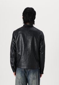 Giubbotto in pelle nera con una trama liscia, dotato di colletto, maniche lunghe e vestibilità sagomata, abbinato a jeans in denim.