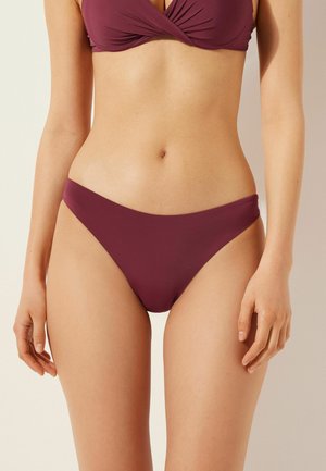 Bas de bikini mauve en matériau lisse et extensible, avec un design taille basse et une couverture minimale, idéal pour la baignade ou la plage.