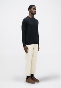 Pulover tricotat bleumarin, pantaloni crem cu manșete răsucite, încălțăminte maro. Design simplu cu o siluetă ajustată și textură netedă.