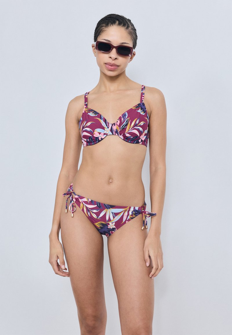 Ensemble bikini violet avec motifs floraux, comprenant des bretelles réglables sur le haut et des côtés noués sur le bas. Texture de tissu lisse.