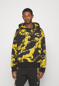 Zwarte katoenen hoodie met een gele barokpatroon en opschrift, lange mouwen, verstelbare koordjes en geribbelde onderrand.