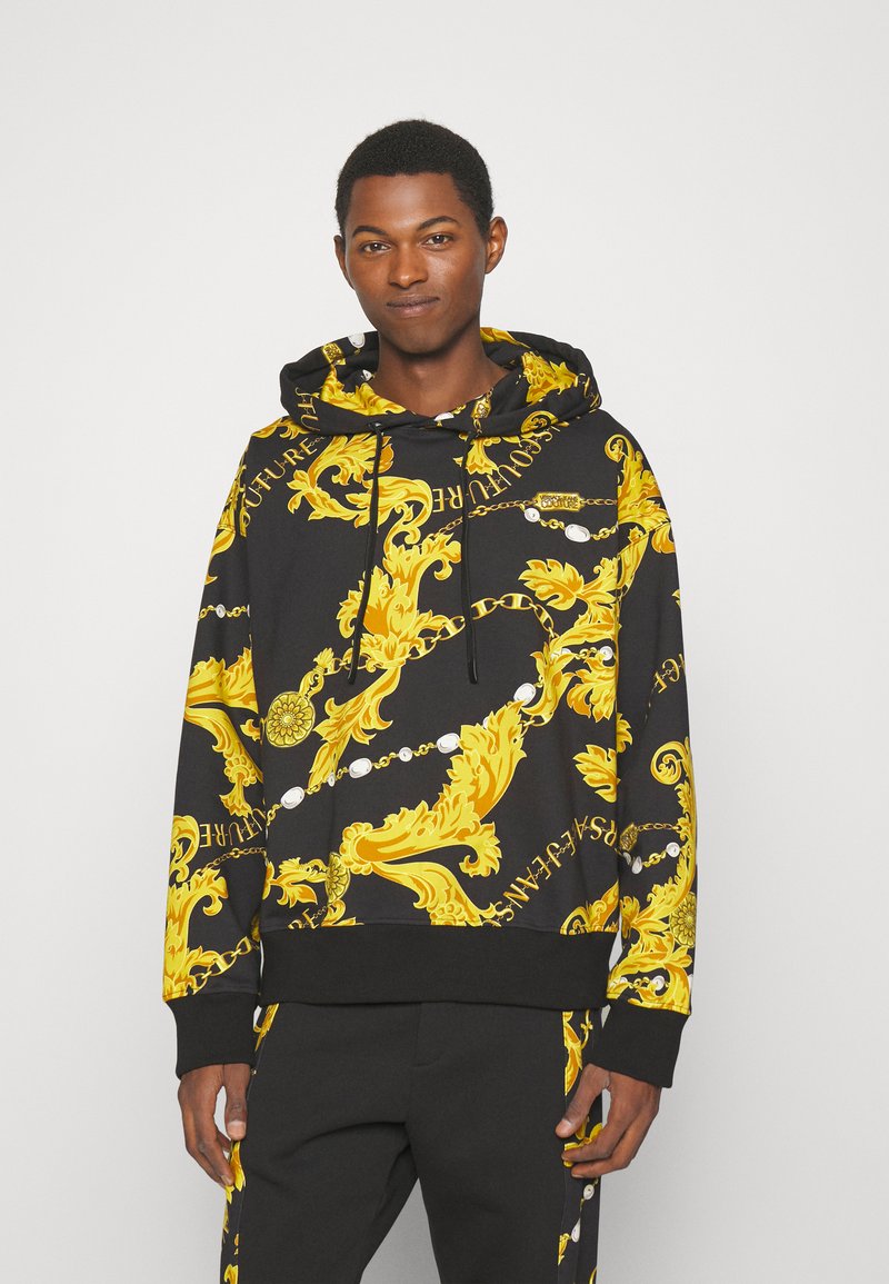 Zwarte katoenen hoodie met een gele barokpatroon en opschrift, lange mouwen, verstelbare koordjes en geribbelde onderrand.