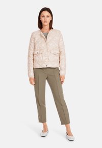 Gepolsterte, hellrosa Jacke mit Rautensteppung und zwei Fronttaschen, kombiniert mit olivgrünen Hosen und gemusterten Slippern.