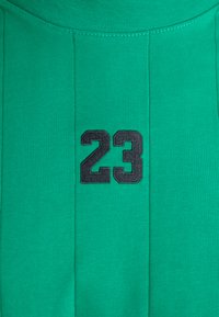 Zeleno rebrasto blago z visokim ovratnikom, ki ima na sprednji strani izstopajoč črn vezen "23". Preprost, teksturiran dizajn.