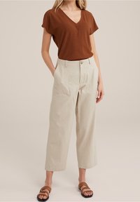 Brun v-ringad topp med subtil zigzag-textur, parat med rymliga beiga byxor med framfickor och knäppning. Bruna strap-sandaler.