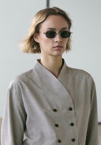 Gestreiftes Hemd zum Knöpfen in Hellgrau und Weiß mit Wickeldesign, breitem Kragen und glatter Textur. Modell trägt Piloten-Sonnenbrille.