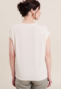 Helles beige Kurzarmoberteil mit lässigem Schnitt, das über eine dezente Rippstruktur und einen abgerundeten Saum verfügt. Keine sichtbaren Logos oder Muster.