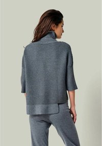 Grauer gerippter Pullover mit hohem Kragen und kurzen Ärmeln, mit einer lockeren Passform und einem längeren Saum hinten. Glatte Textur und modernes Design.