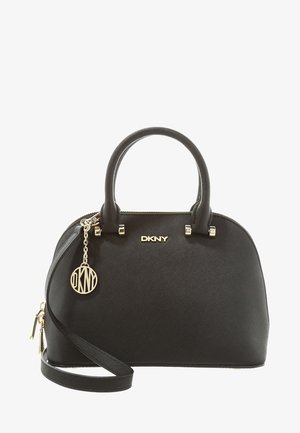 Sac à main DKNY noir en forme de dôme avec deux poignées, une bandoulière amovible et un pendentif logo doré suspendu à une des poignées.