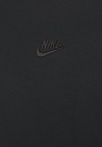 Černé bavlněné tričko s malým černým vyšívaným logem Nike na hrudi. Hladká textura s přiléhavým střihem.