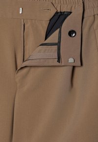 Pantalones marrones con una textura suave, que presentan un bolsillo con cremallera, cinturilla elástica y detalles de forro interior negro en contraste.