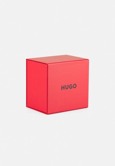 Boîte en carton rouge avec une finition mate, arborant un logo noir "HUGO" sur le devant, de forme carrée, avec des bords nets et un design épuré.